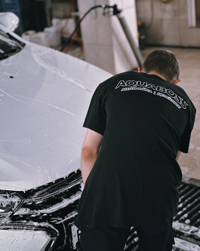 Professional cleaning a white car with foam in an auto garage.