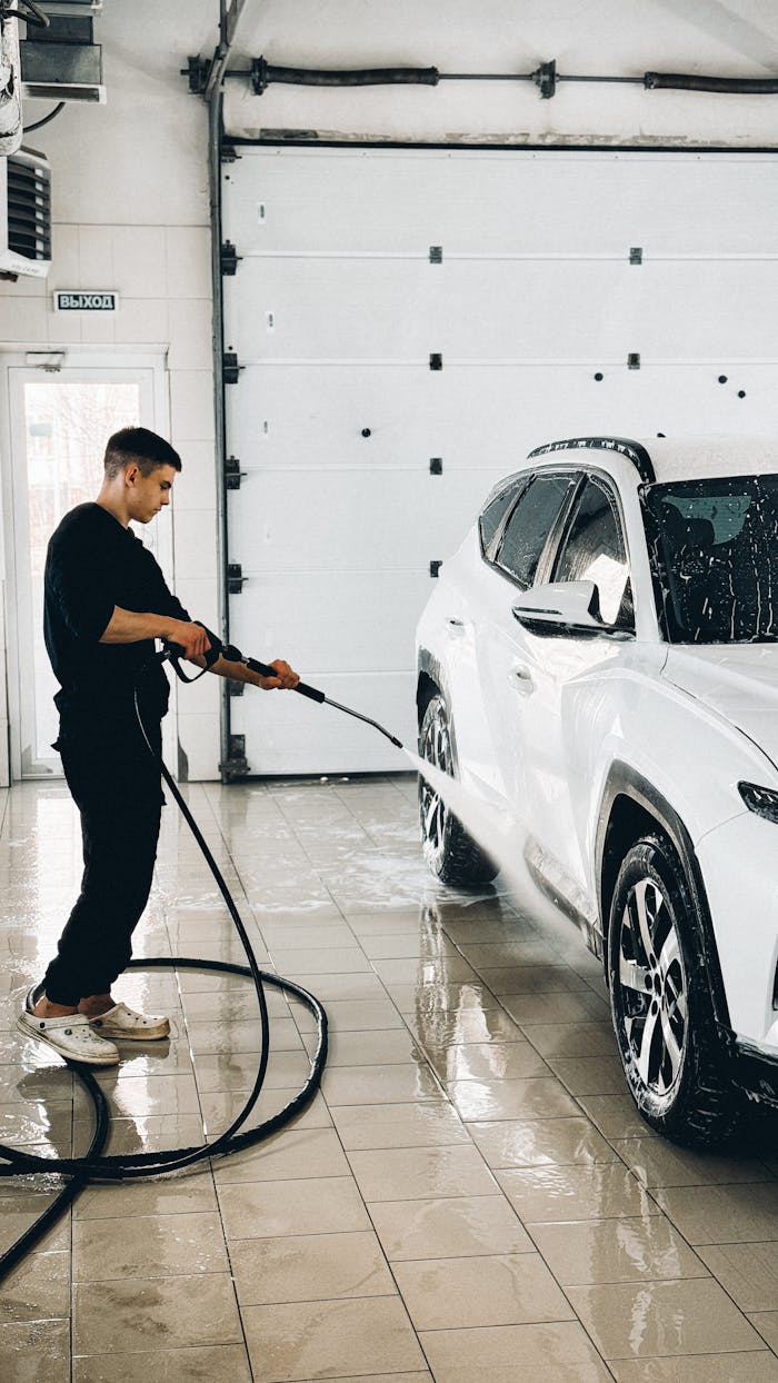 Man using a power washer to clean a car in a garage setting.